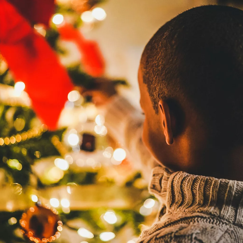 Bild zu Spendenprojekt Winterwunderland. Kind mit einem Christbaum im Hintergrund. 